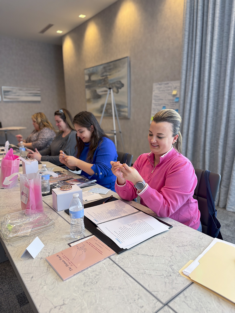 Women seated at a table making bracelets at a Breast Cancer Awareness event