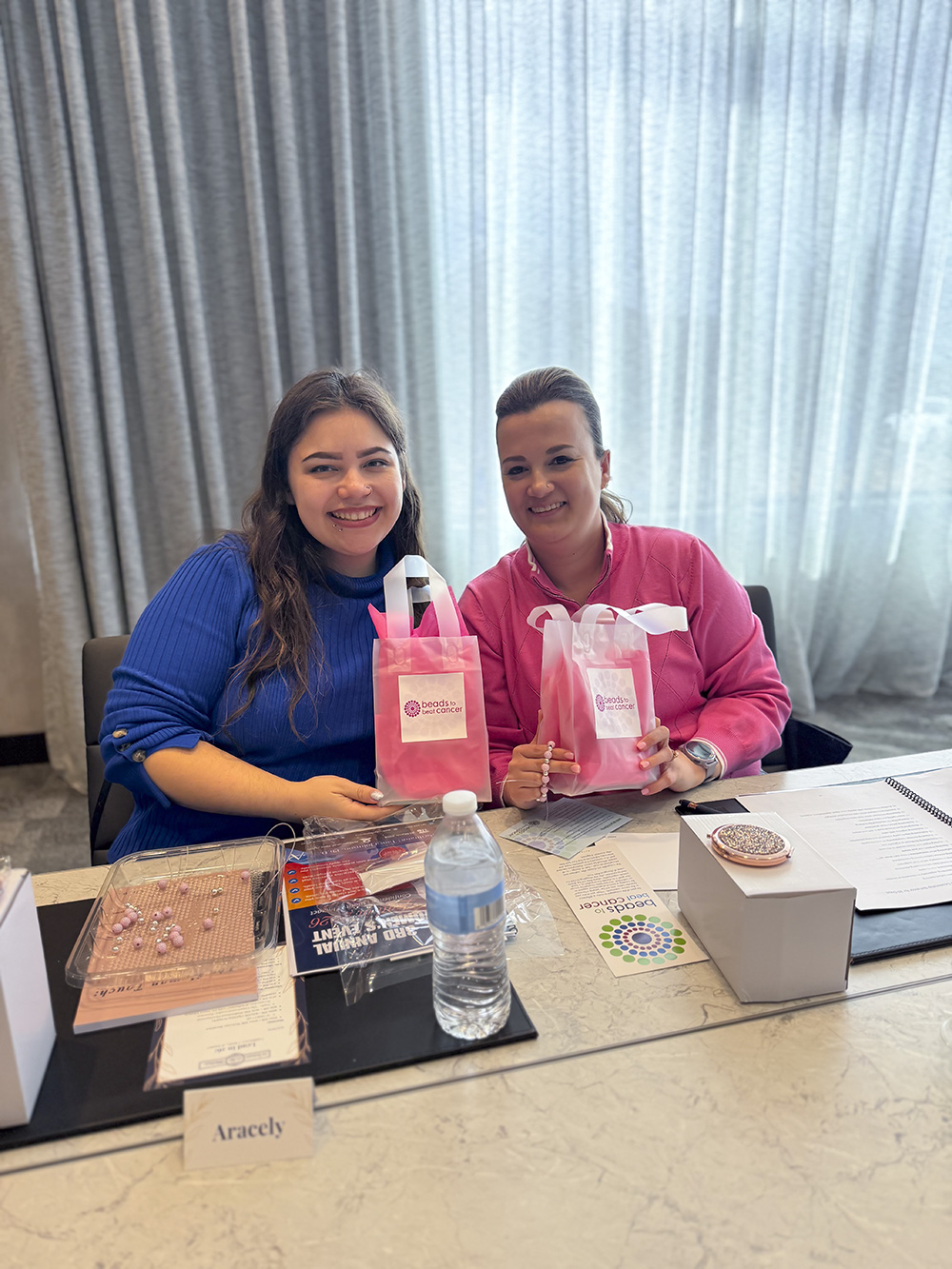 Two women holding pink Beads to Beat Cancer gift bags at a Breast Cancer Awareness event