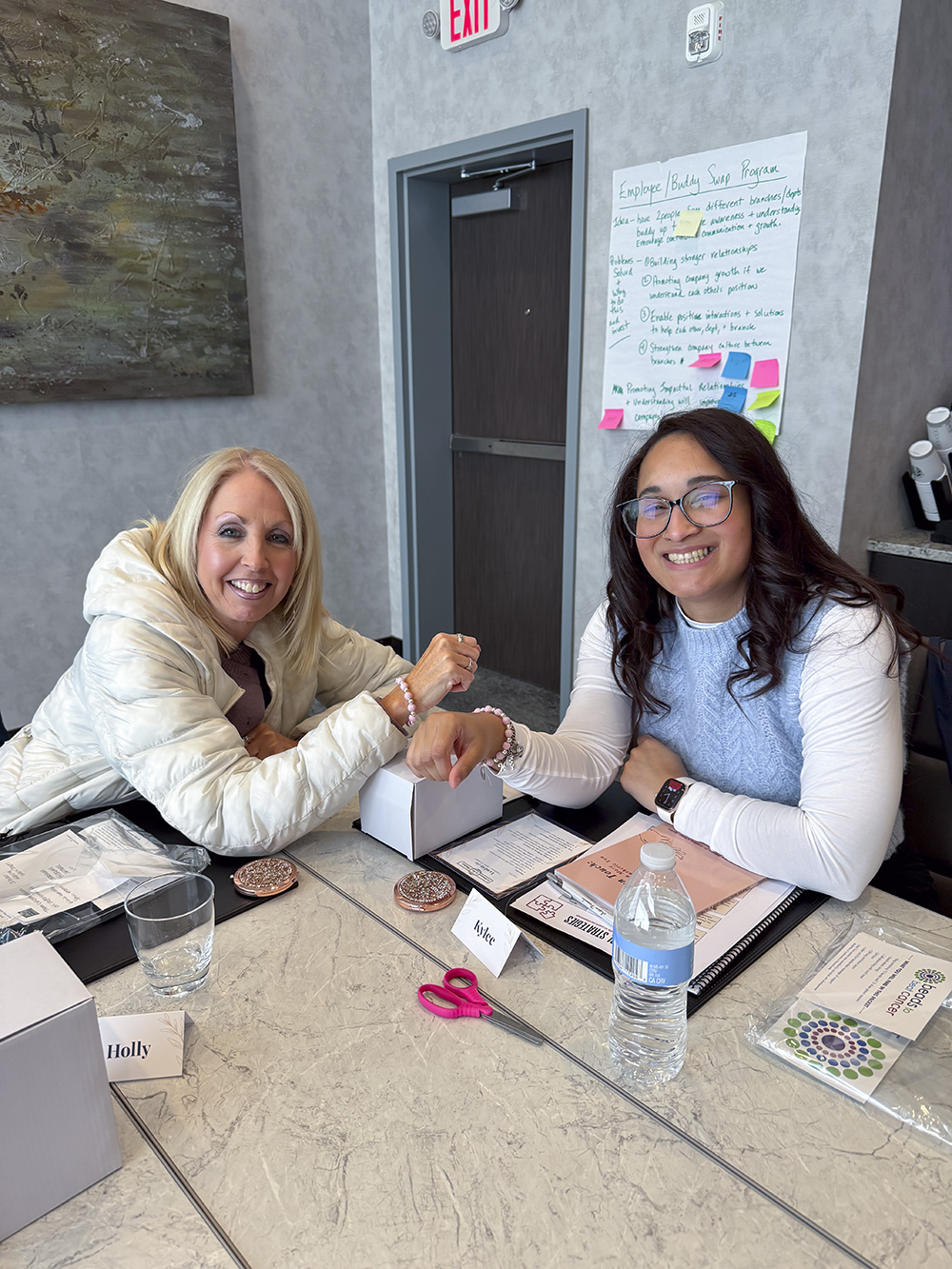 Two women working on bracelets together at a Breast Cancer Awareness event