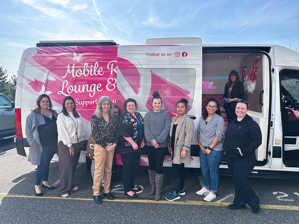 Group of employees posing in front of the Mobile B Lounge truck at a Breast Cancer Awareness event
