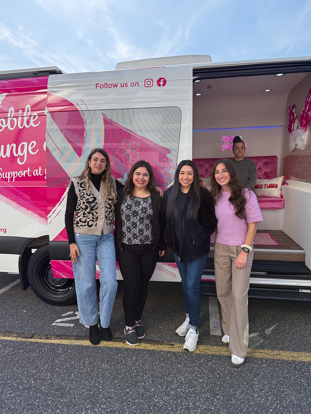 Four women posing in front of the Mobile B Lounge truck at a Breast Cancer Awareness event